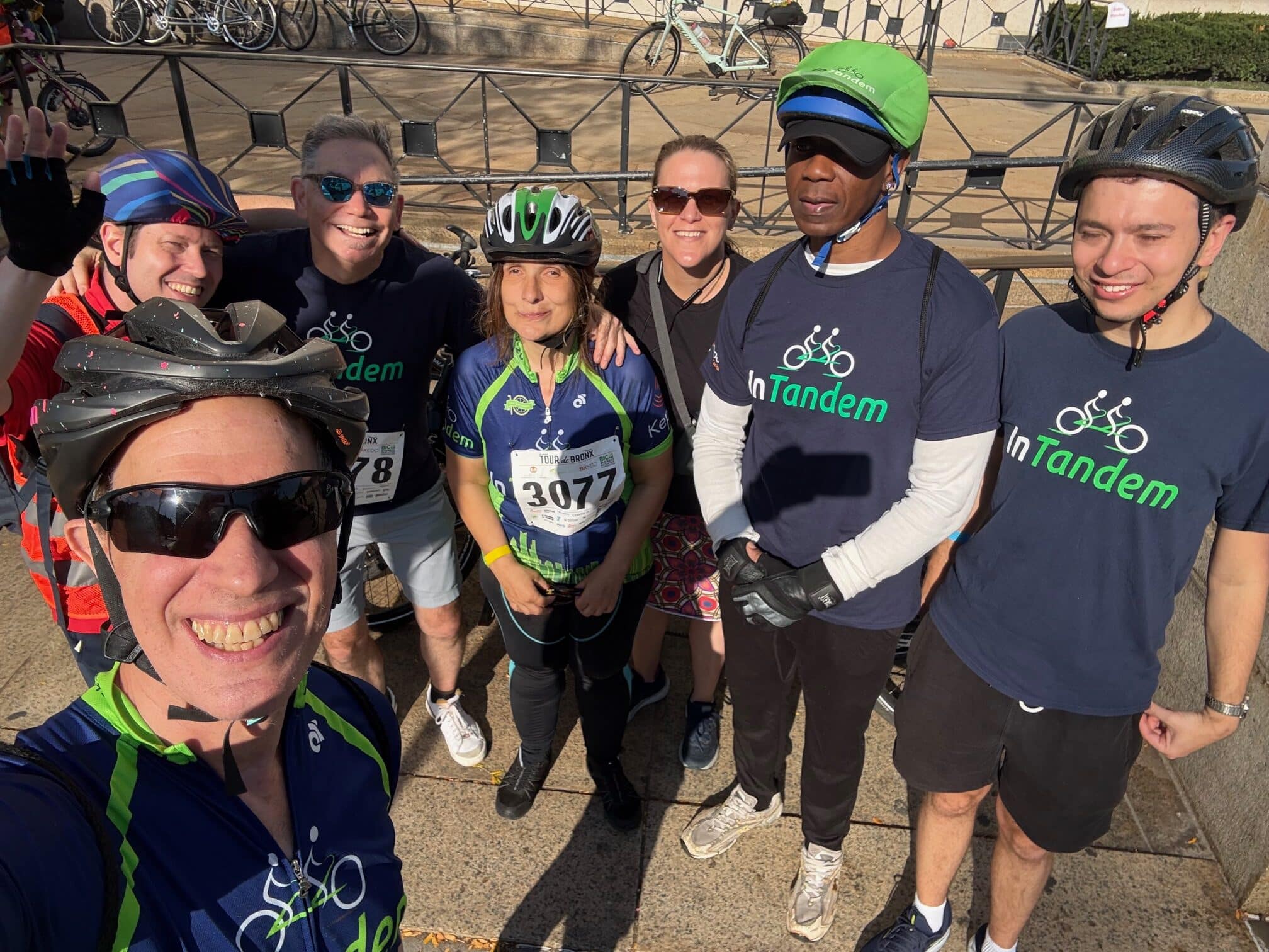 A group of cyclists in team gear and helmets pose for a selfie outdoors.
