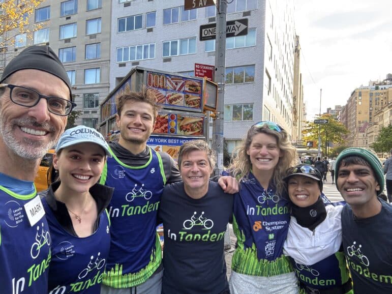 Seven smiling InTandem Cycling runners and supporters take a selfie on Fifth Avenue at the NYC Marathon.
