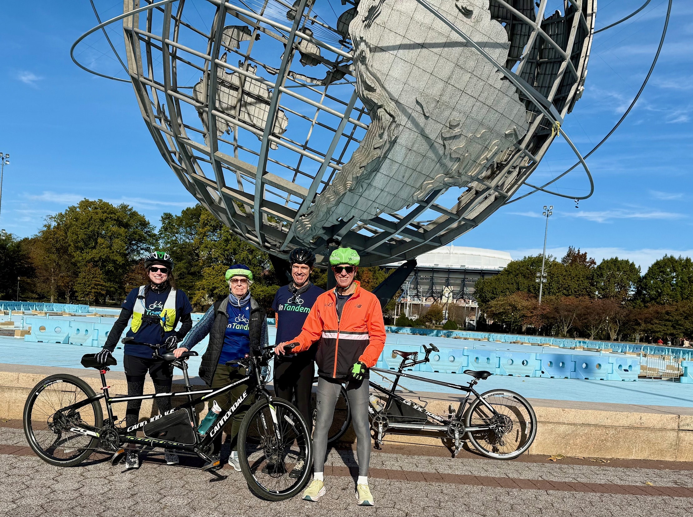 Four InTandem Cycling riders pose with two tandem bikes in front of the Unisphere in Queens.